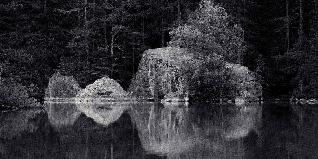 Rochers avec reflet dans l'eau d'un lac, apparence de glace en noir blanc